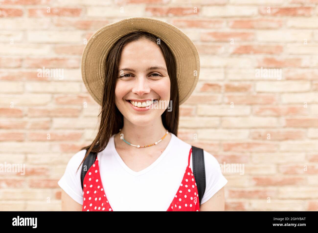 Young female tourist smiling while looking at camera in front of wall ...