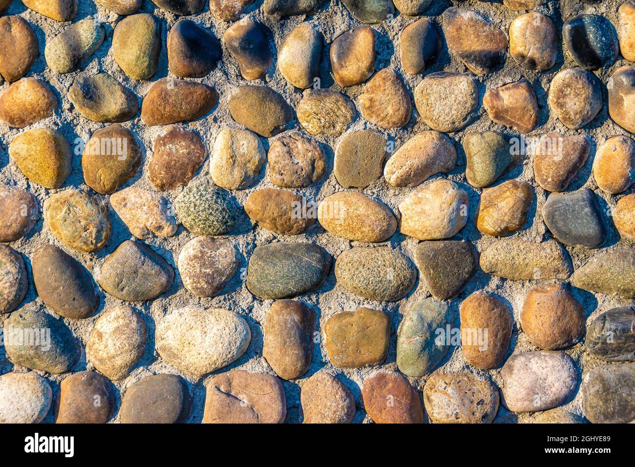 multi-colored and multi-textured pebble stones lie in rows partially pressed into the main covering of a horizontal or vertical surface Stock Photo