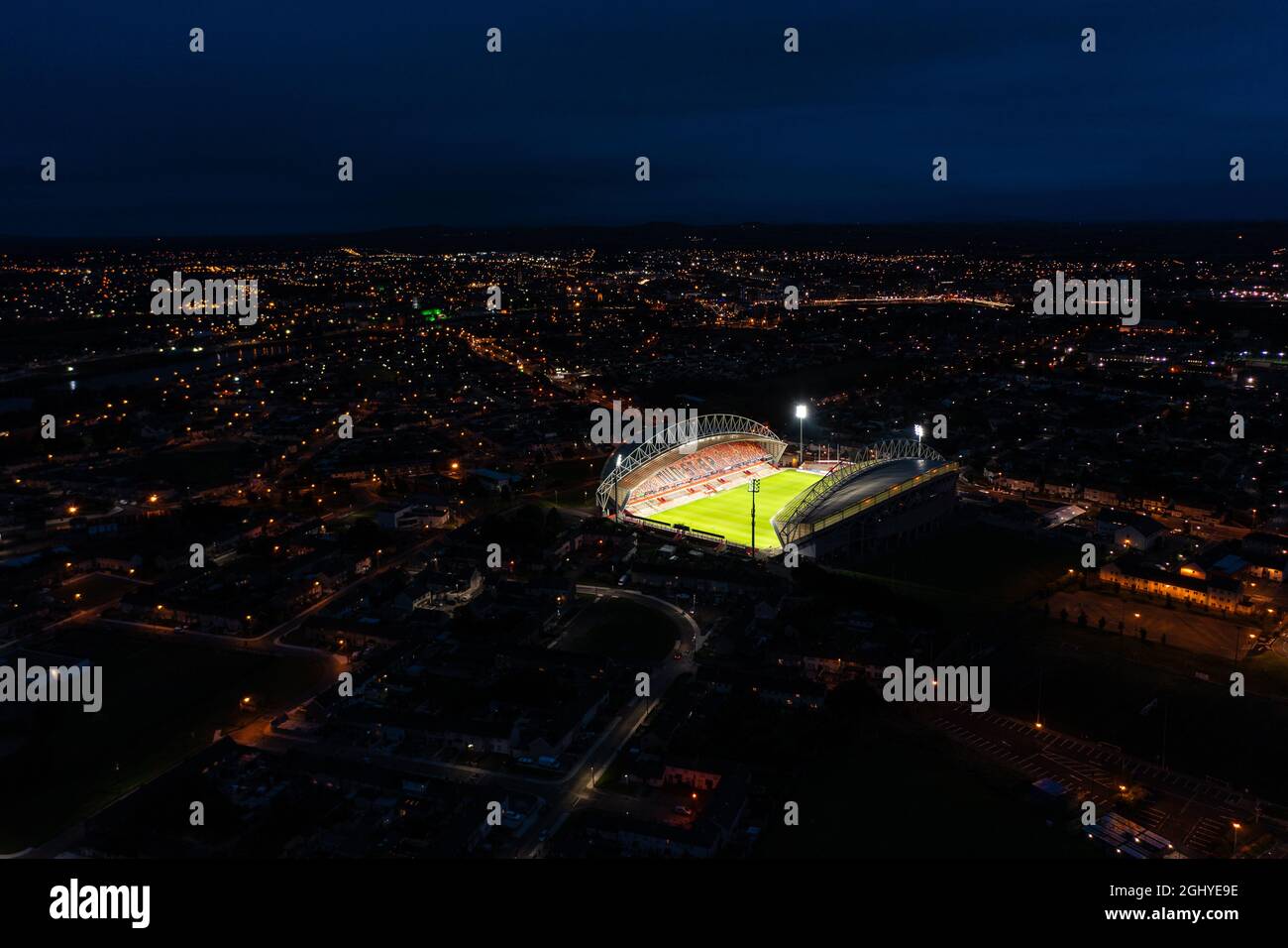 Aerial view of stadium with green grass pitch and focus lights on in Ireland surrounded by residential house in city at night Stock Photo