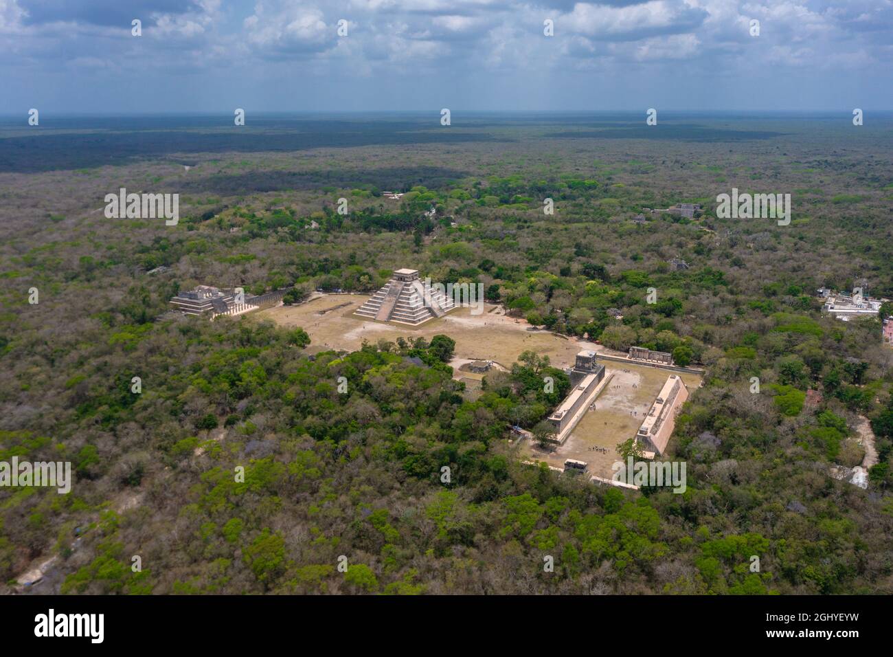 Aerial view of the beautiful Chicen Itza and Mayan Pyramid in Mexico surrounded with ground and greenery with ocean under cloudy sky during day Stock Photo