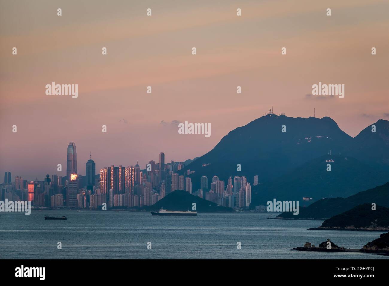 The setting sun reflected in highrise buildings on Hong Kong Island, with a pink sky due to the 'Belt of Venus' phenomenon Stock Photo