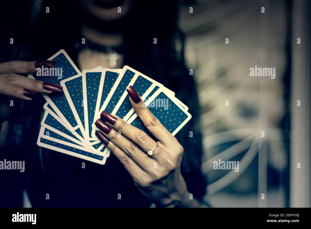 Blurry backside ofTarot cards in hand with red nails.Fortune teller  in Halloween night. Low light Horror screen moment with film grain.And Cross proc Stock Photo