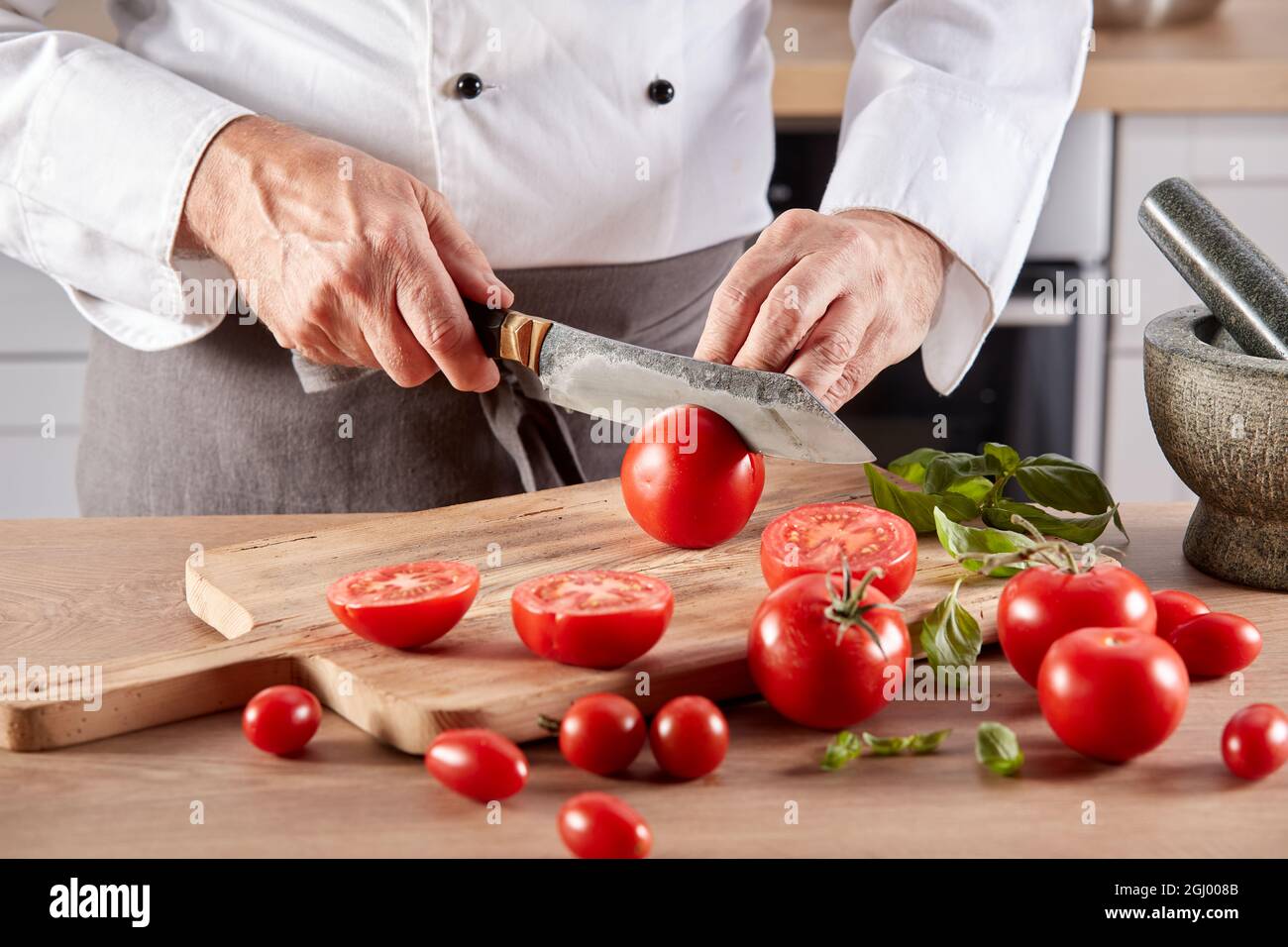 Anonymous crop male chef cutting fresh tomatoes on wooden chopping