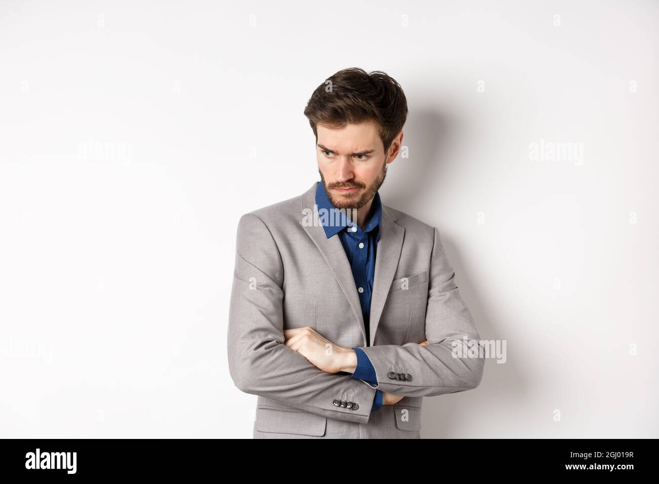 Moody guy in suit looking aside with unfair face, cross arms on chest ...