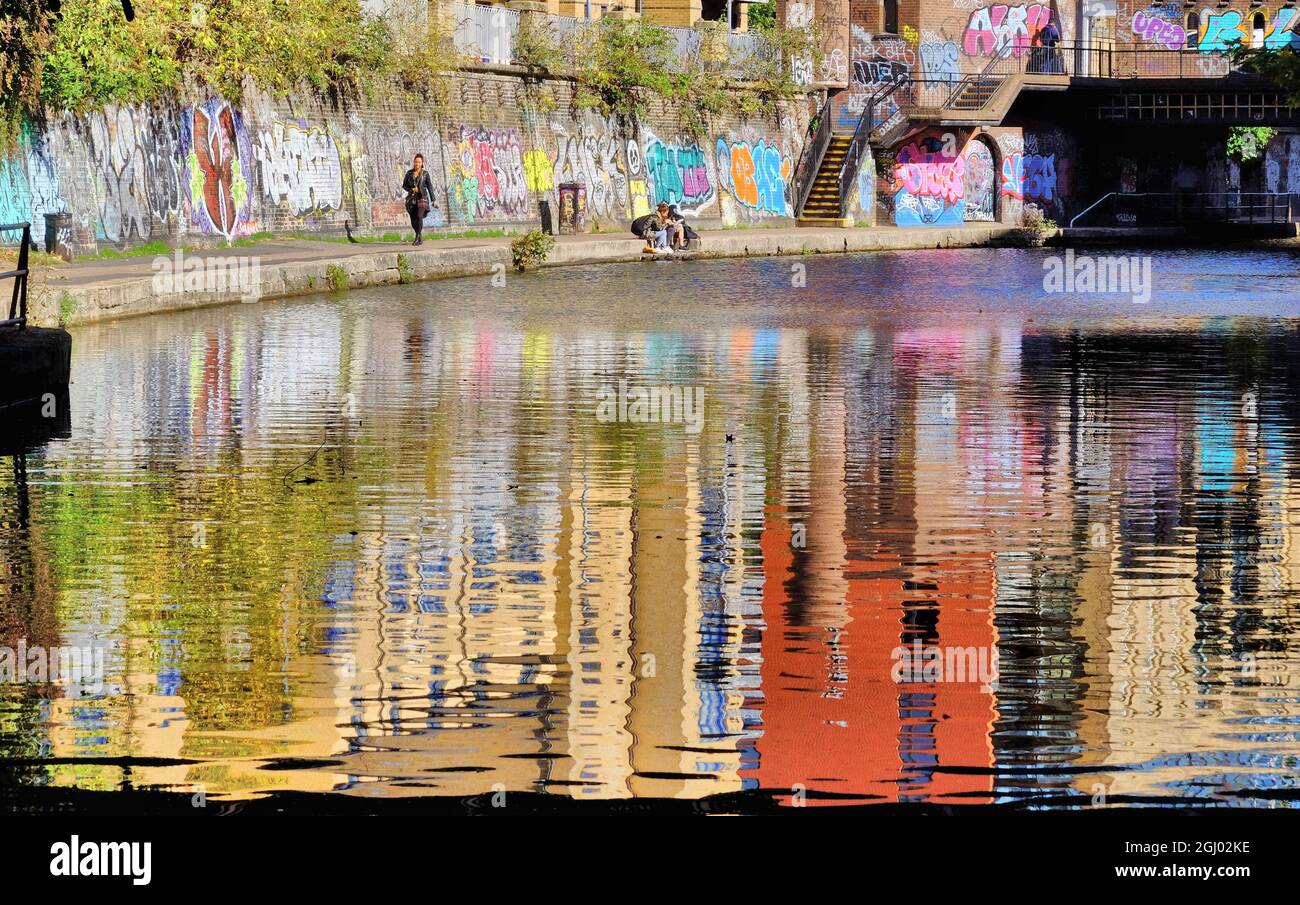 Brightly coloured graffiti and reflections of buildings along Regent’s Canal in Camden Town, London, England Stock Photo