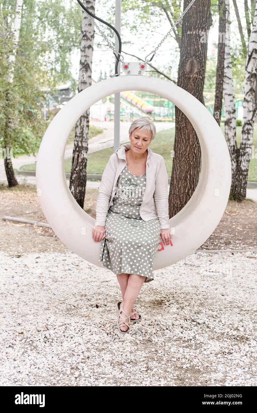 Sad caucasian senior woman sitting on round bench in park Stock Photo ...