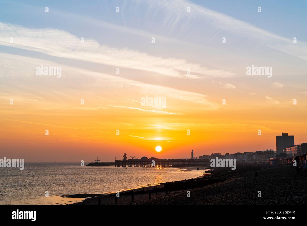 The sun rising into an orange sky over the silhouette of the pier in ...