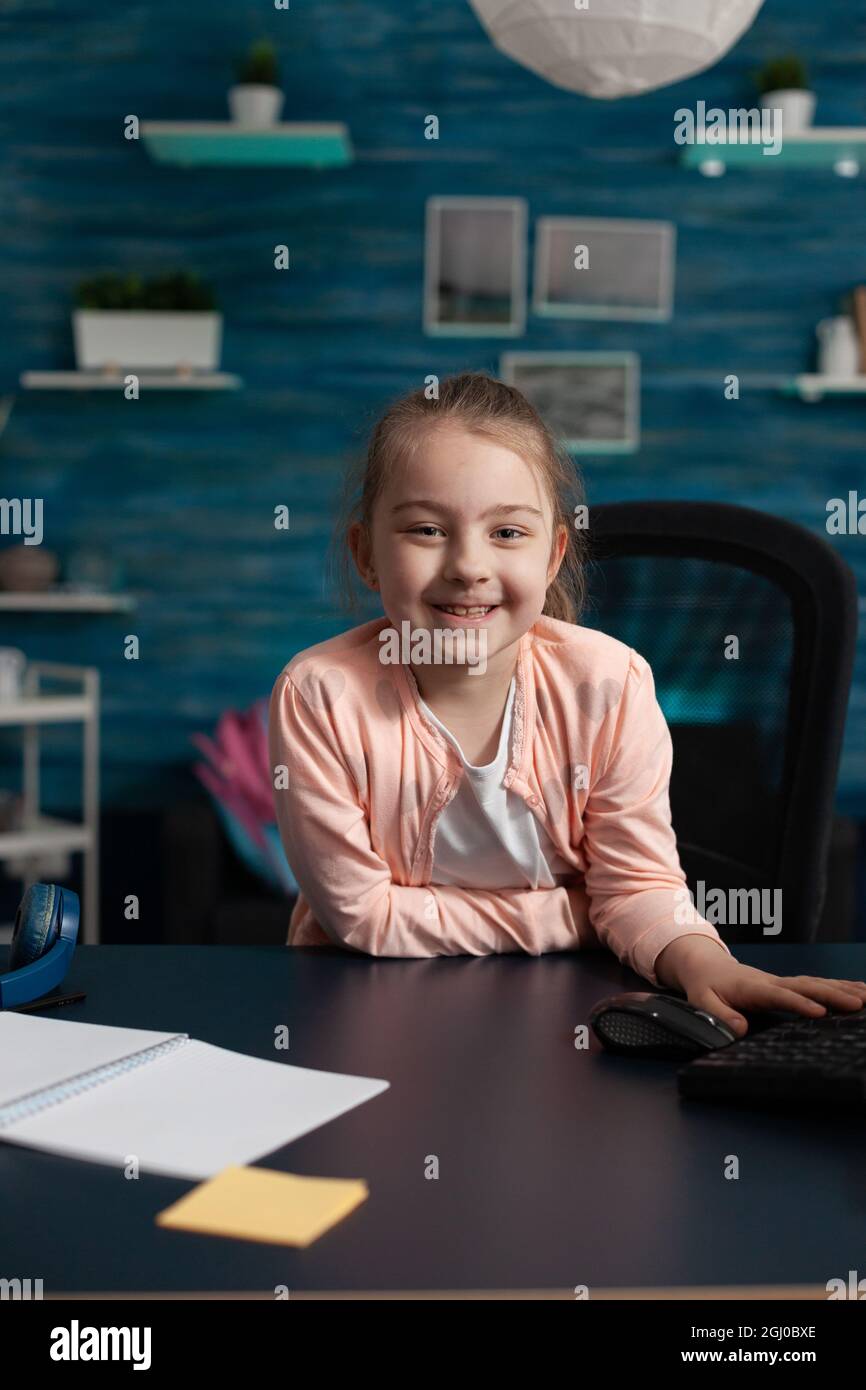 Joyful little girl smiling sitting at desk for online school work on