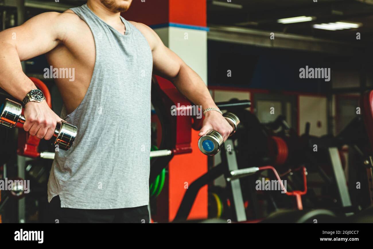 young male athlete performs exercises in the gym with dumbbells ...