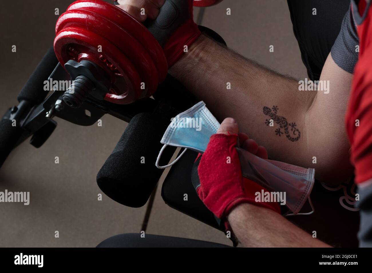 Man's arm with a lizard tattoo working out with a dumbbell and holding a facemask in the other hand Stock Photo