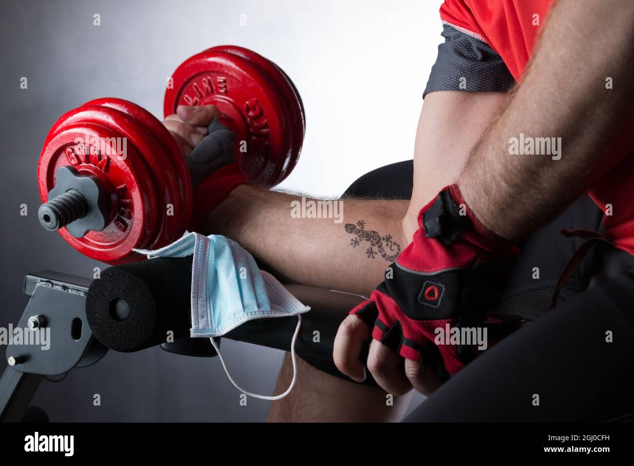 Man's arm with a lizard tattoo working out with a dumbbell during the pandemic Stock Photo
