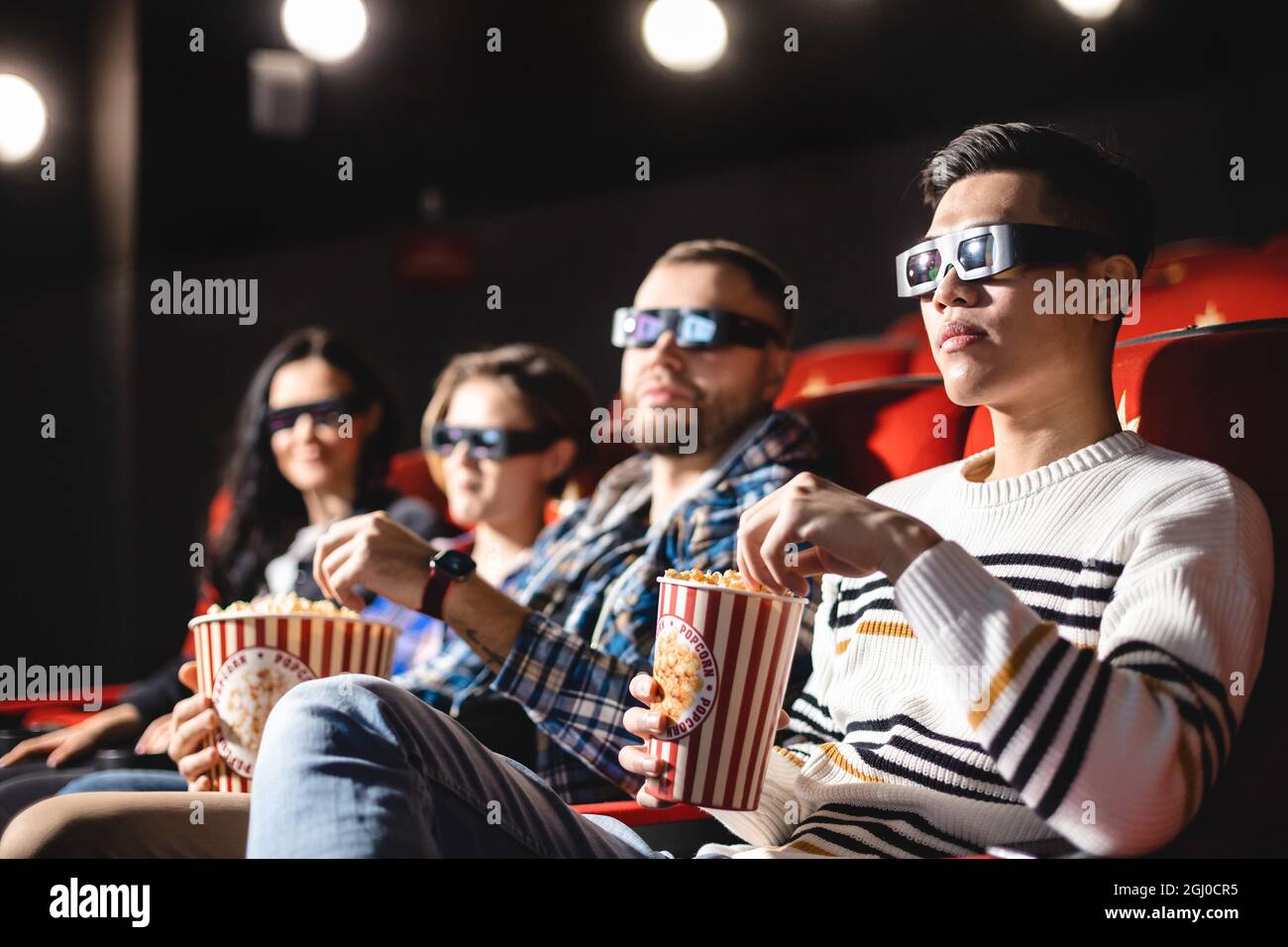 Friends are watching a movie in the cinema. People sit in the armchairs of the cinema and look at the screen with special glasses for 3D Stock Photo