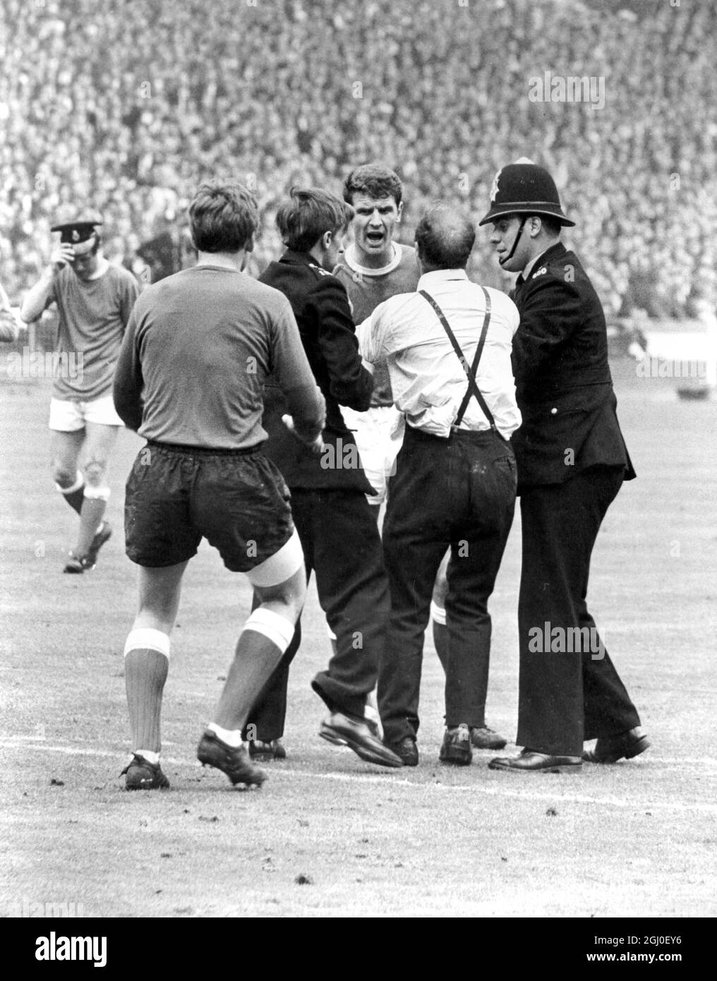 1966 FA Cup Final Everton v Sheffield Wednesday Just another one of those madly enthusiastic moments during the FA Cup Final at Wembley, London, as a supporter who is too keenly enthusiastic rushed on the field after the hero of the match Mike Trebilcock had scored Everton's second goal. As police remove the supporter Everton captain Brian Labone remonstrates with him (Labone facing camera). On left, with back to camera is Gordon West, and extreme left, trying on the police officer's hat for size, is Brian Harris. 14th May 1966 Stock Photo