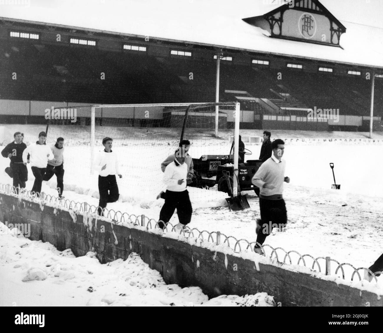 Tottenham Hotspur train in the snow - Spurs players, headed by Maurice Norman, getting in some running practice at their White Hart Lane ground whilst groundsmen are seen busily clearing the snow in an effort to get the ground clear for the Spurs cup tie versus Burnley. The cup holders played Burnley in the final last year. 1st January 1963 Stock Photo