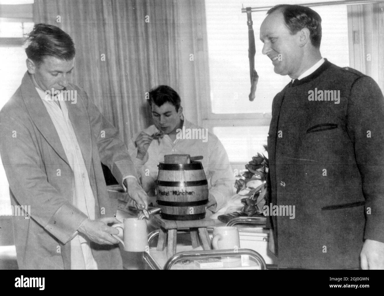 Munich, Germany: Manchester United's Bobby Charlton (left), and his team-mate Ken Morgans (seated on his bed in hospital) can be seen to be on the road to recovery. Inn Keeper Hans Gross can be seen to be beaming broadly as he brings the two players a sample of Munich beer. Feburary 10th 1958 Stock Photo