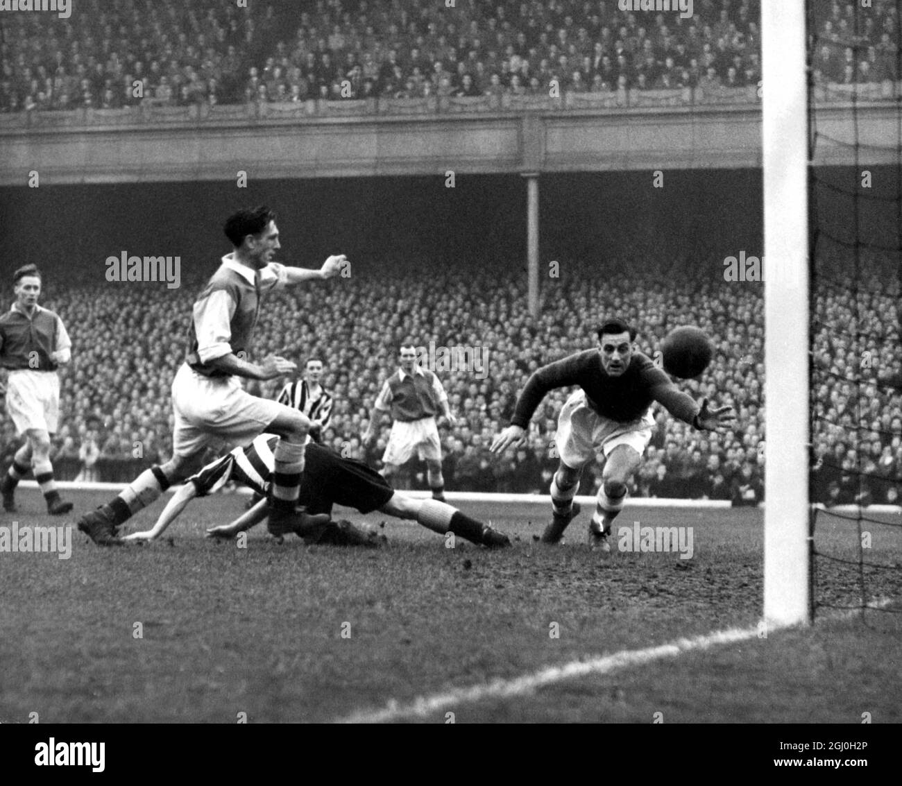 The goal scored by Newcastle to beat the Arsenal at Highbury Stadium. Hair, the Newcastle outside left (seen in background striped shirt) kicked for goal, but it was diverted by Milburn (on ground) to Mercer's shin from which it cannoned into the net despite a great effort by Swindin. The other two players in the picture are Macar (extreme left) and Barnes (in background) - 20th November 1948 Stock Photo