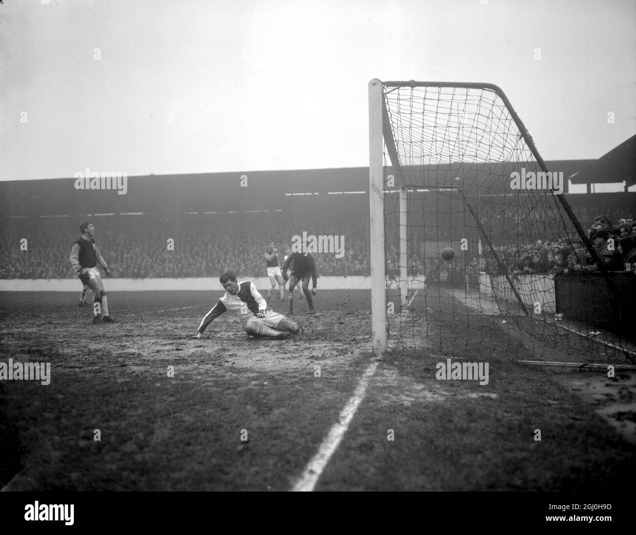London: mud-caked West ham goalkeeper Jim Standen (Dark Jersey and Shorts), looks dismayed as the ball enters the net for Blackburn's third goal at today's Boxing Day soccer match at Upton Park, London. E. The goal was scored by Andy McEvoy, who is seen falling on the rain soaked pitch after making his successful head in effort. 26 December 1963 Stock Photo