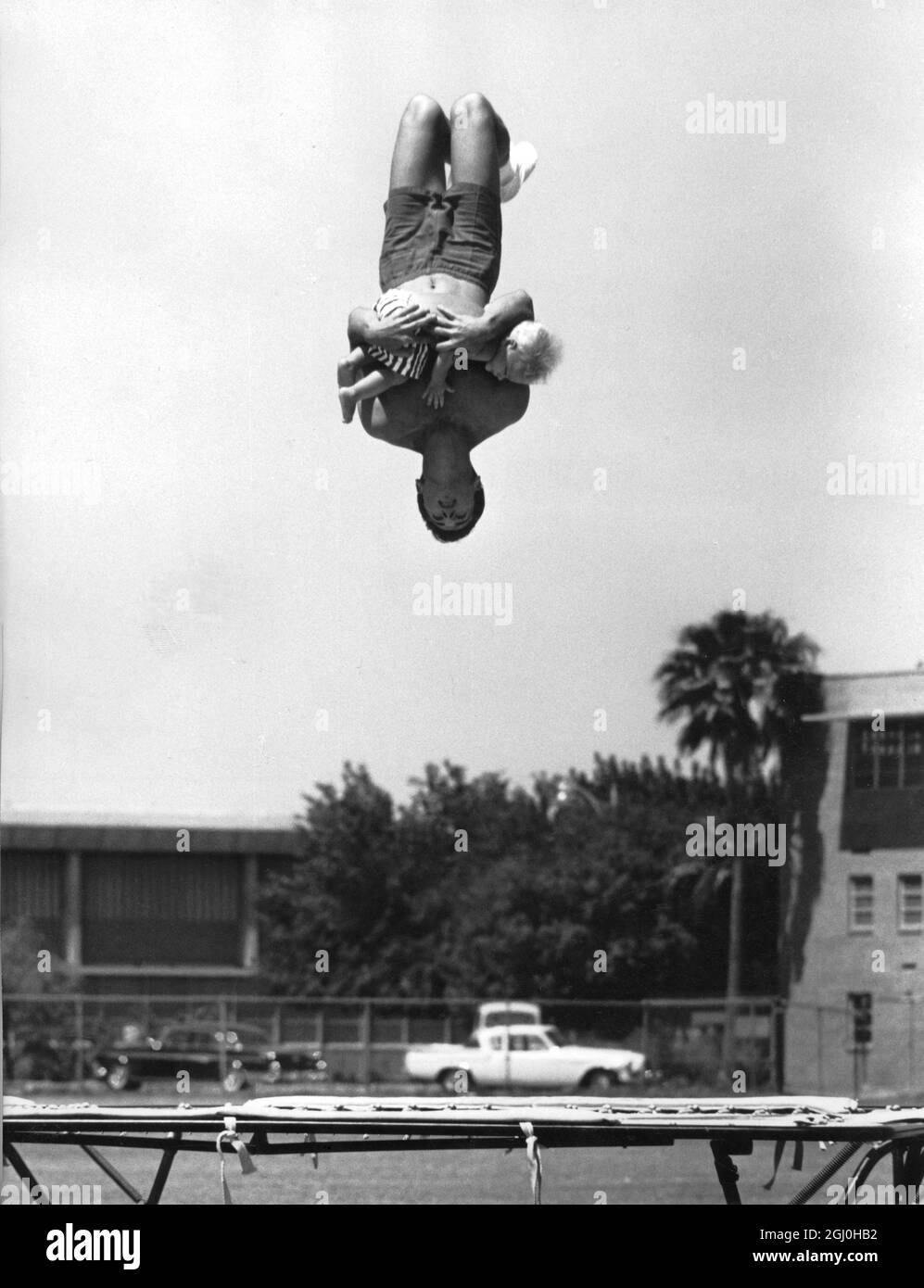 Harvey Plant carefully cradles his son in his arms while doing a back flip on the trampoline. Danny has complete confidence in his father and shows no fear during these high-flying somersaults. 1964 *** Local Caption *** High-flying father and son Stock Photo