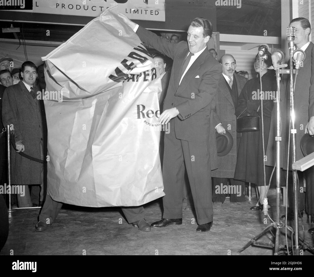 London Freddy Mills sets out to prove that the saying current in boxing circles - ' he couldn't punch his way out of a paper bag' doesn't apply where he is concerned. With television star Eamonn Andrews, standing by, Freddie begins his onslaught on the large size bag. It happened at Olympia, London today at a preview of the Packaging Exhibition which opens tomorrow. 19 January 1953 Stock Photo