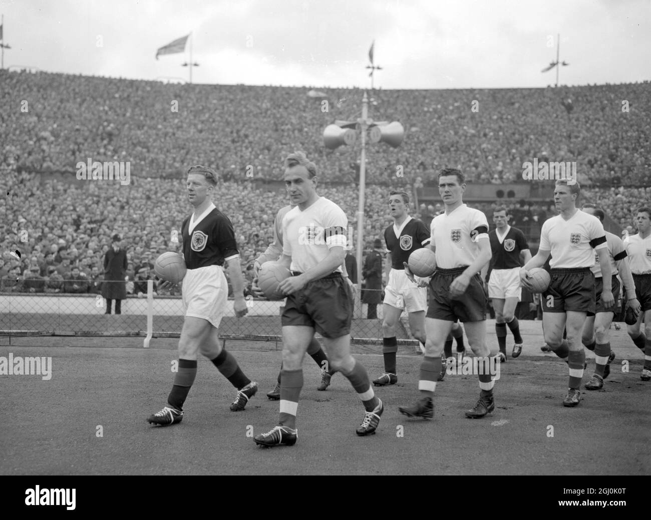 London: Walking onto the lush green turf of Wembley stadium, wolves and England Captain Billy Wright (white shirts, leading) receives the applause of the crowd at this his 100th game for England. Bobby Evans, (dark shirt) leads out the Scottish Team. The players are wearing black arm-bands, in mourning for Jeff Hall, Birmingham City and England full-back who died of Polio recently. 11 April 1959 Stock Photo