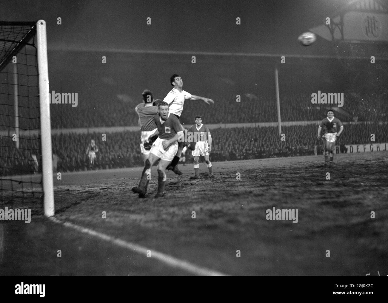 London: In their fourth- round replay of the F.A. Cup played under floodlights tonight, Tottenham Hotspurs beat Crewe Alexandra by thirteen goals to two. Here, Crewe goalkeeper Evans jumps for the ball during a Tottenham attack with Crewe defender Willmott (No.5) and Spurs centre- forward R. Smith (Highest). 3 February 1960 Stock Photo