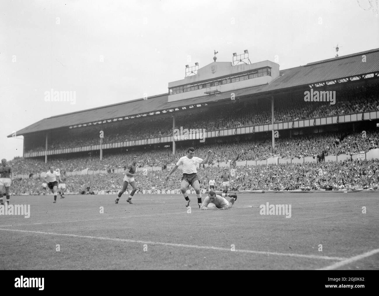 London: FA Selection XI goalie Springett dives to the ground to get the ball as Spurs centre-forward Bobby Smith gets ready for a kick at the goal during the 'Spurs-FA Selection friendly game at White Hart lane this afternoon. 'Spurs, the FA Cup winners and League Championship winners, won 3 -2. 12 August 1961 Stock Photo