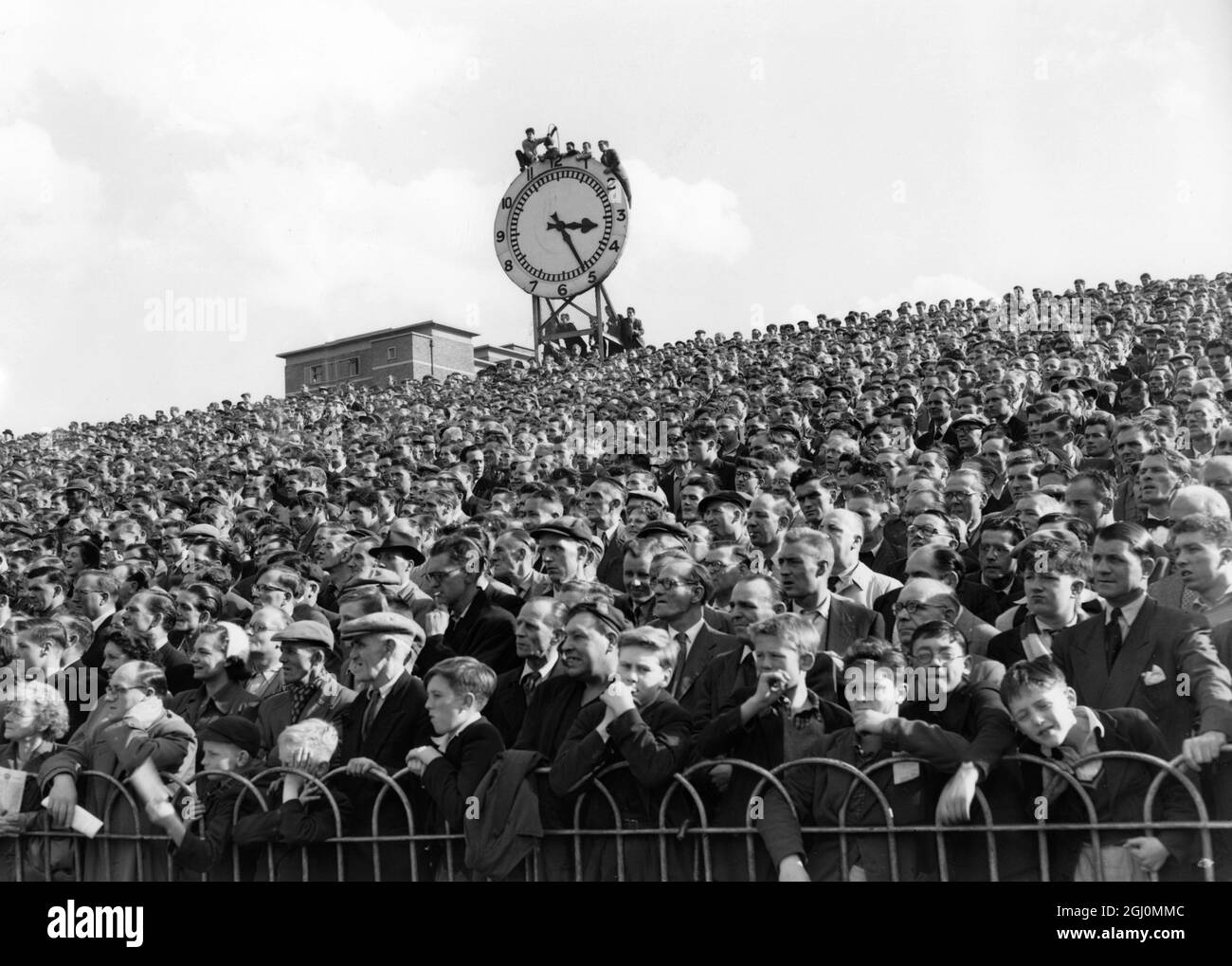 Keen on seeing every incident of the game , these soccer fans climbed on to the clock at the Highbury ground , gaining an uninterrupted vantage point during Arsenal's home match against Manchester United 29th September 1956 Stock Photo