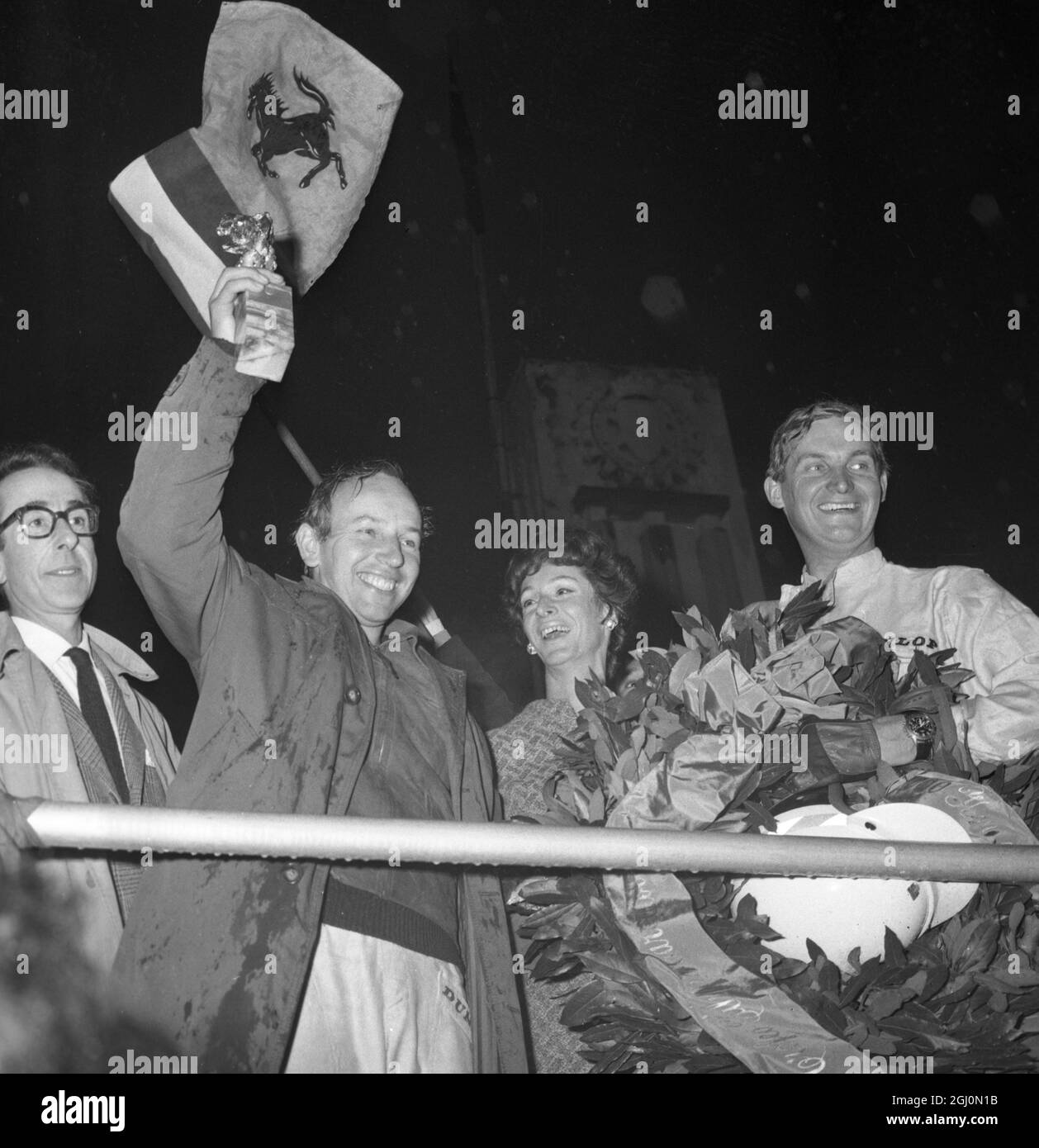 John Surtees smiles as he waves his trophy from the Victory Rostrum after he had won the 1000 km race in his Ferrari 300-P2 prototype at Monza April 25th. In the centre is the Countess Caracciolo widow of the former president of the Automobile club of Italy. 1966 Stock Photo