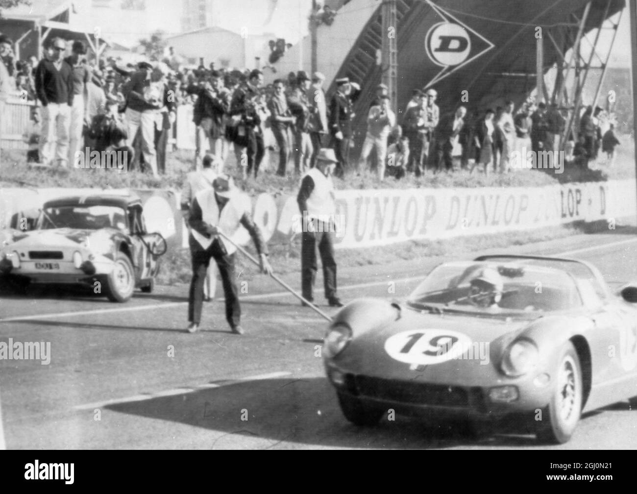 John Surtees in his Ferarri leading after 33 laps flashing past Mike Rothschild's crumpled Triumph Spitfire which crashed into the wall, after it is thought a tyre blew. 20 June 1964 Stock Photo