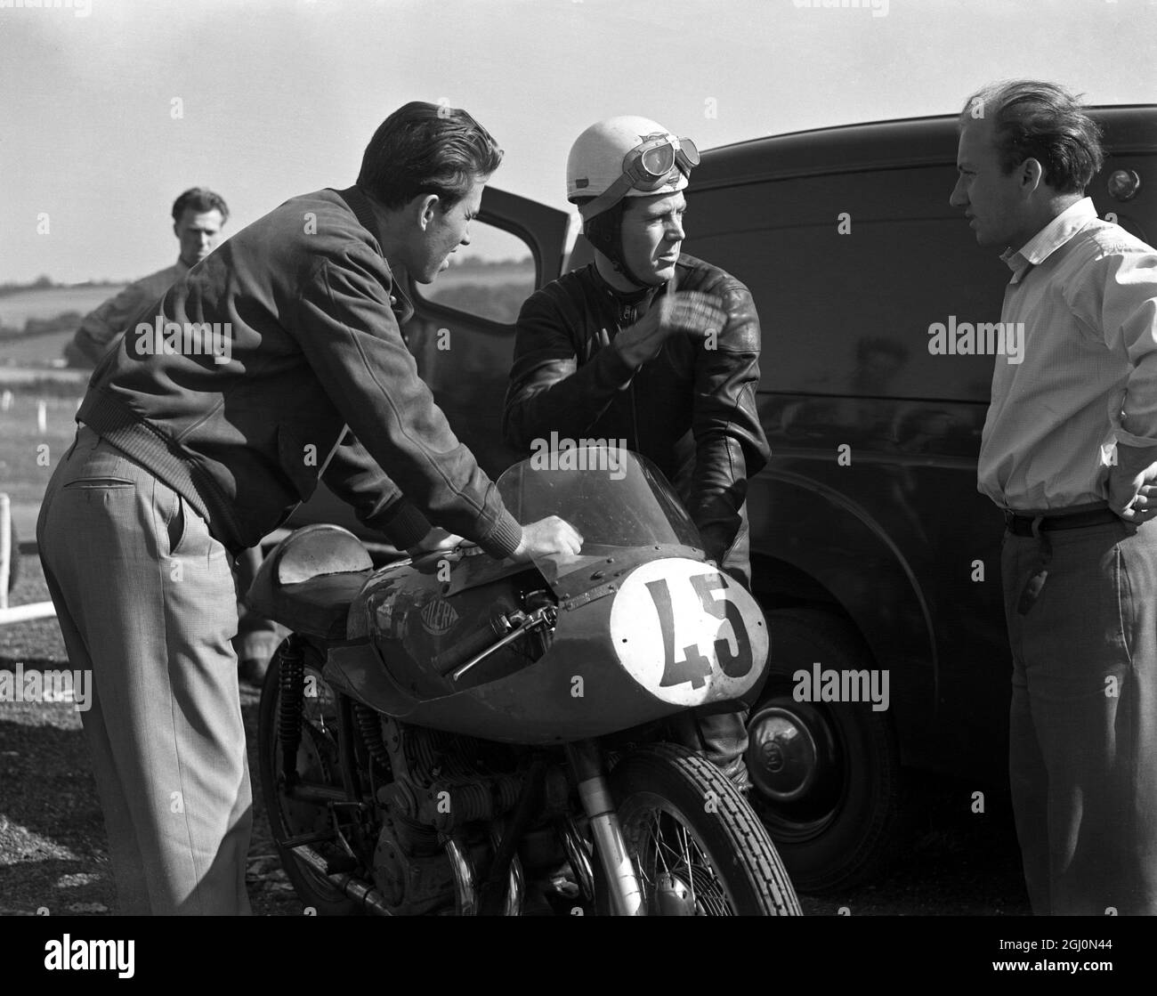 Geoff Duke , British world road racing motorcycle champion , talking with his mechanics during a break in practise at the Brands Hatch racing circuit in Kent . 24th September 1955 Stock Photo