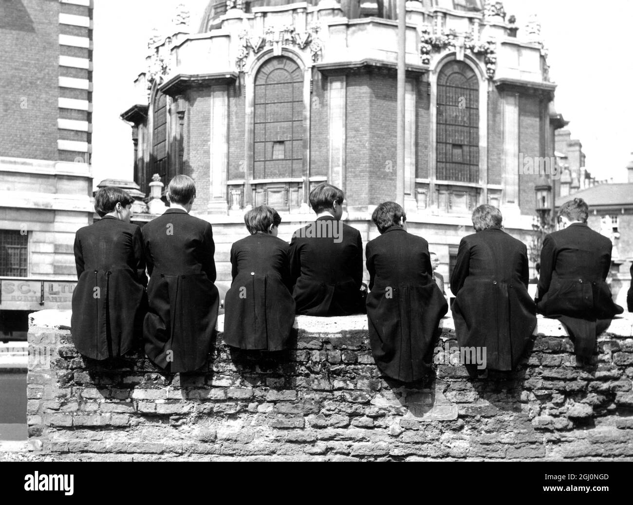 Back view of the tail - coats worn by school boys of Eton College who sat on a school wall today waiting for their parents and other members of their families , who were attending the ' Fourth of June ' festivities , which include speeches in Latin , cricket matches and processions of boats on the River Thames . 1965 Stock Photo