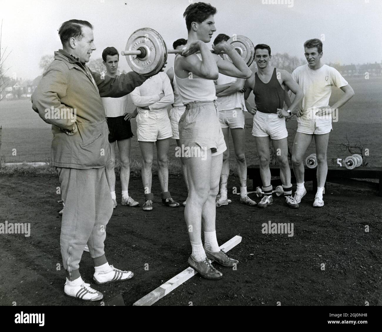 Southern Area AAA coach John Le Masurier of Worcester Park , instructs a group of young athletes at the London University Sports Ground , Motspur Park , Surrey , England . Weight training to his instruction may be seen with 17 year old Clarks College student Tony Tymms of Richmond . 4 January 1961 Stock Photo