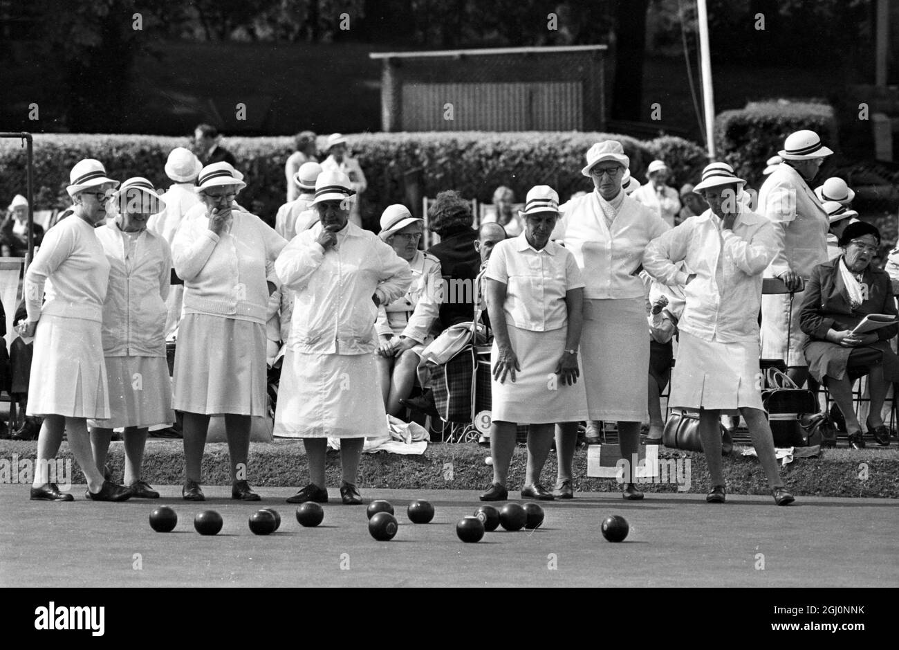 A woman raises her arm after her wood hit the jack or white ball as other members of her team look on , at the Amateur National Championships of the English Women's Bowling Association at Wimbledon Park , London , England . 25 August 1969 Stock Photo