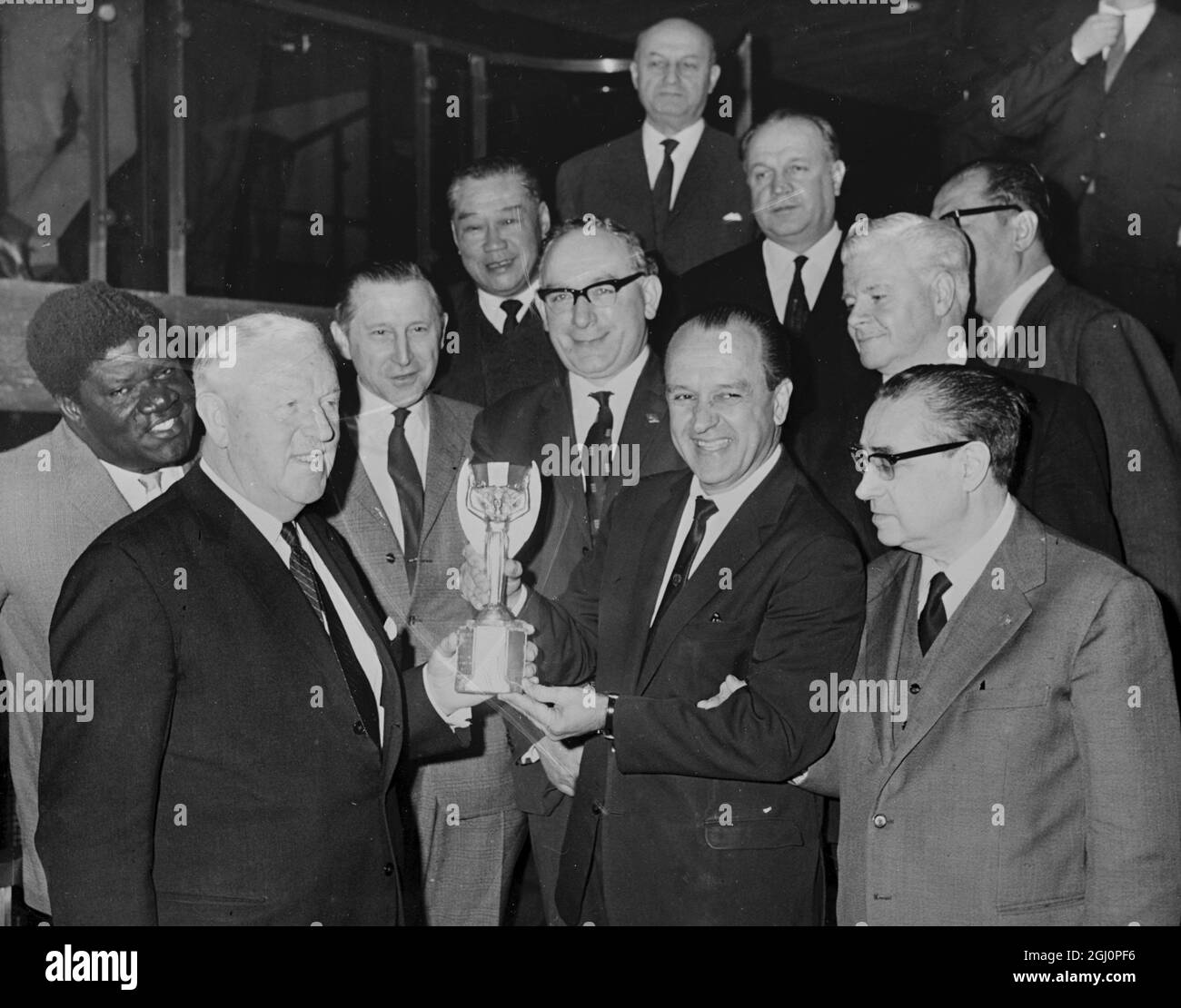 Dr Luiz Murgel , delegate for Brazil , current holders of the world soccer cup , hands over the coveted Jules Rimet trophy to Sir Stanley Rous (left ) , President of FIFA , after the world trophy had arrived in London today . The watching delegates are from right : Dr Ottorino Barassi (Italy) ; Jim Maguire (in rear, white hair) , of USA ; Harry Cavan (centre, glasses) , of Northern Ireland ; Lim Zee Siong (in rear) , of Malaya , and Dr Helmet Kaeser (next to Mr Cavan) , General Secretary , FIFA . The world cup football tournament takes place in the United Kingdom in July 5 January 1966 Stock Photo