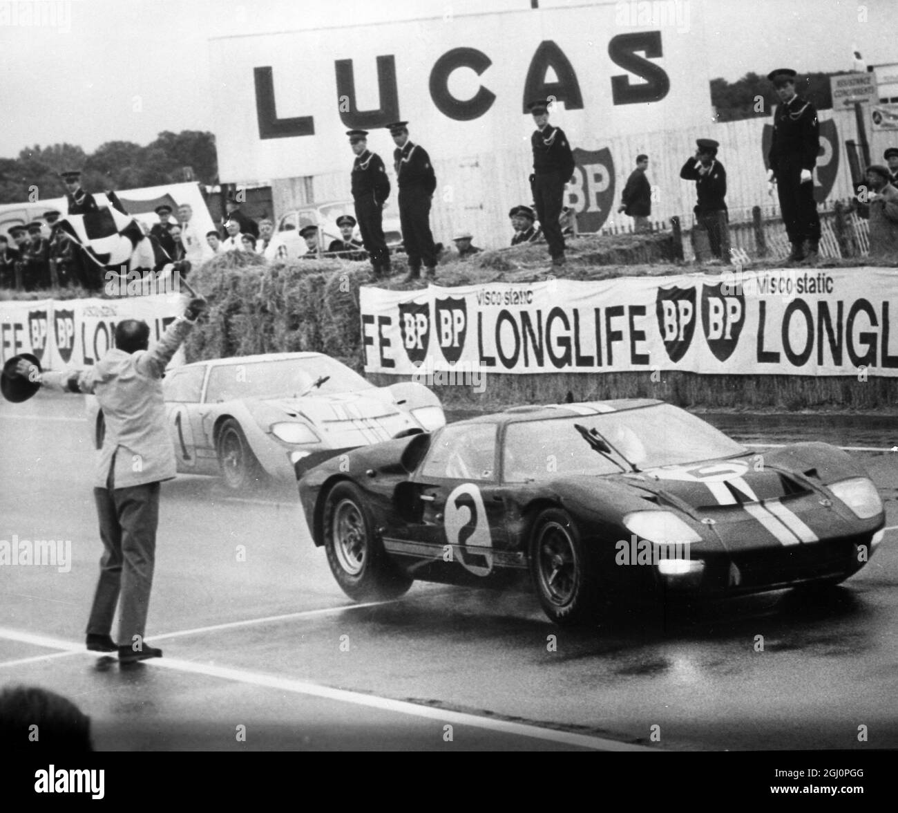 Official final placings in the 24-hour sports car race were in No 2 Ford , Bruce McLaren and Chris Amon of New Zealand , shown here crossing the finishing line . Roy Lunn , British designer of the winning Fords said , '' We tried to make it a dead heat and we forgot about the starting position rule , The McLaren car officially won by 20 metres (60 ft) because that was the distance which separated it from the No 1 car on the starting grid '' . The winner officially average 201.795 kmph for the whole disatance , the first time the 200 km mark had ever been broken . 19 June 1966 Stock Photo