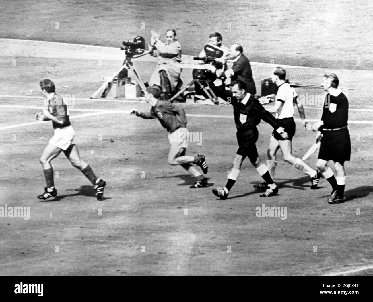 Controvesial Third Goal. Swiss referee Gottfried Dienst points to the middle of the field indicating that he is allowing the controvesial third goal for England scored by Geoff Hurst during yesterday's World Cup Final against West Germany. Two England players are seen racing off to join jubilant team mates. The ball hit the crossbar and rebounded down. All the England players claimed the ball has crossed the line. After consulting the Russian Linesman, the referee allowed the goal. 30 July 1966 Stock Photo