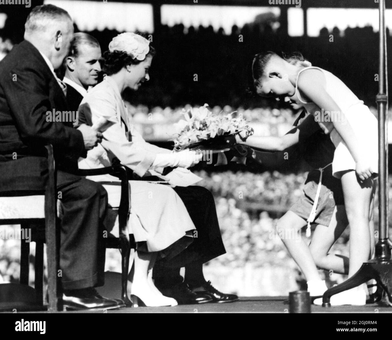 ROYAL AUSTRALIAN TOUR QUEEN RECEIVES A POSY IN MELBOURNE. THE QUEEN accepts a posy from BEVERLEY EMSLEY (10) and TREVOR REES (8) at gathering of ex-servicemen and women at the Melbourne Cricket Ground. On left is RSL State President N.D. WILSON. 3 March 1954 Stock Photo
