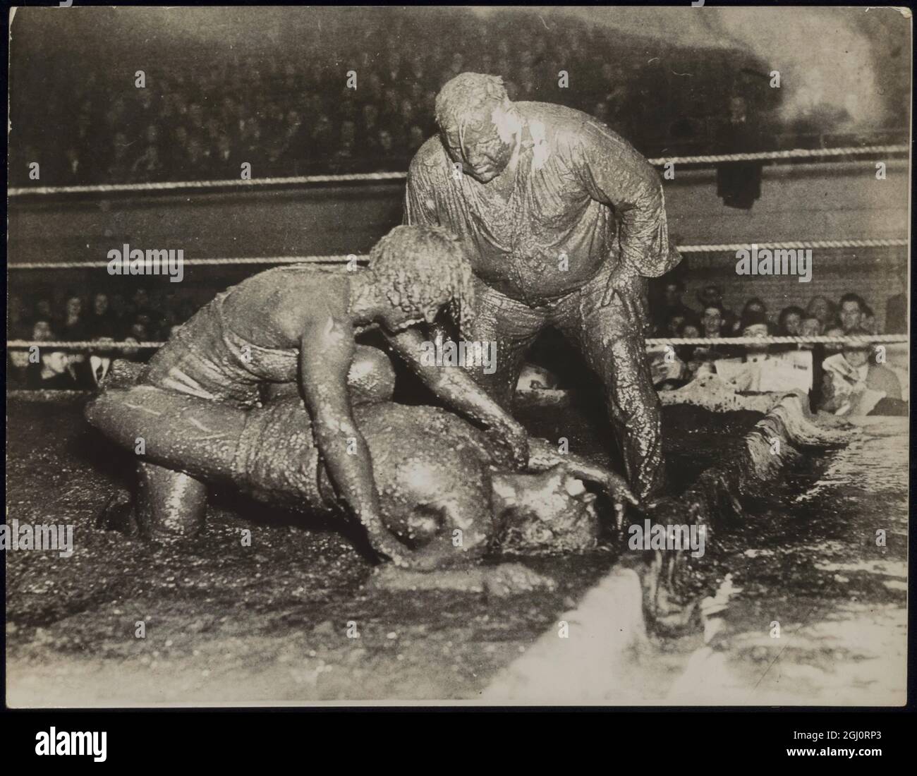 THESE GIRLS LIKE EXERCISE WITH THEIR ''MUD PACK''! Mildred (Cyclone) Burke of Kansas City, Missouri, claimant to the women's wrestling championship of the world, end Leona (Babe) Gordon of Chicago gave each other a mud pack ''treatment'' when they took pert in a Hindu-style wrestling match in a mud-filled ring at Akron, Ohio. Miss Burke scored a one-fall victory. PHOTO SHOWS:- Mildred (Cyclone) Burke (on top) pins her equally muddy opponent, Leone (Babe) Gordon, in the viscous mess as Ernie Maddock, the referee, is about to tap Miss Burke on the shoulder to declare her the winner. The referee Stock Photo
