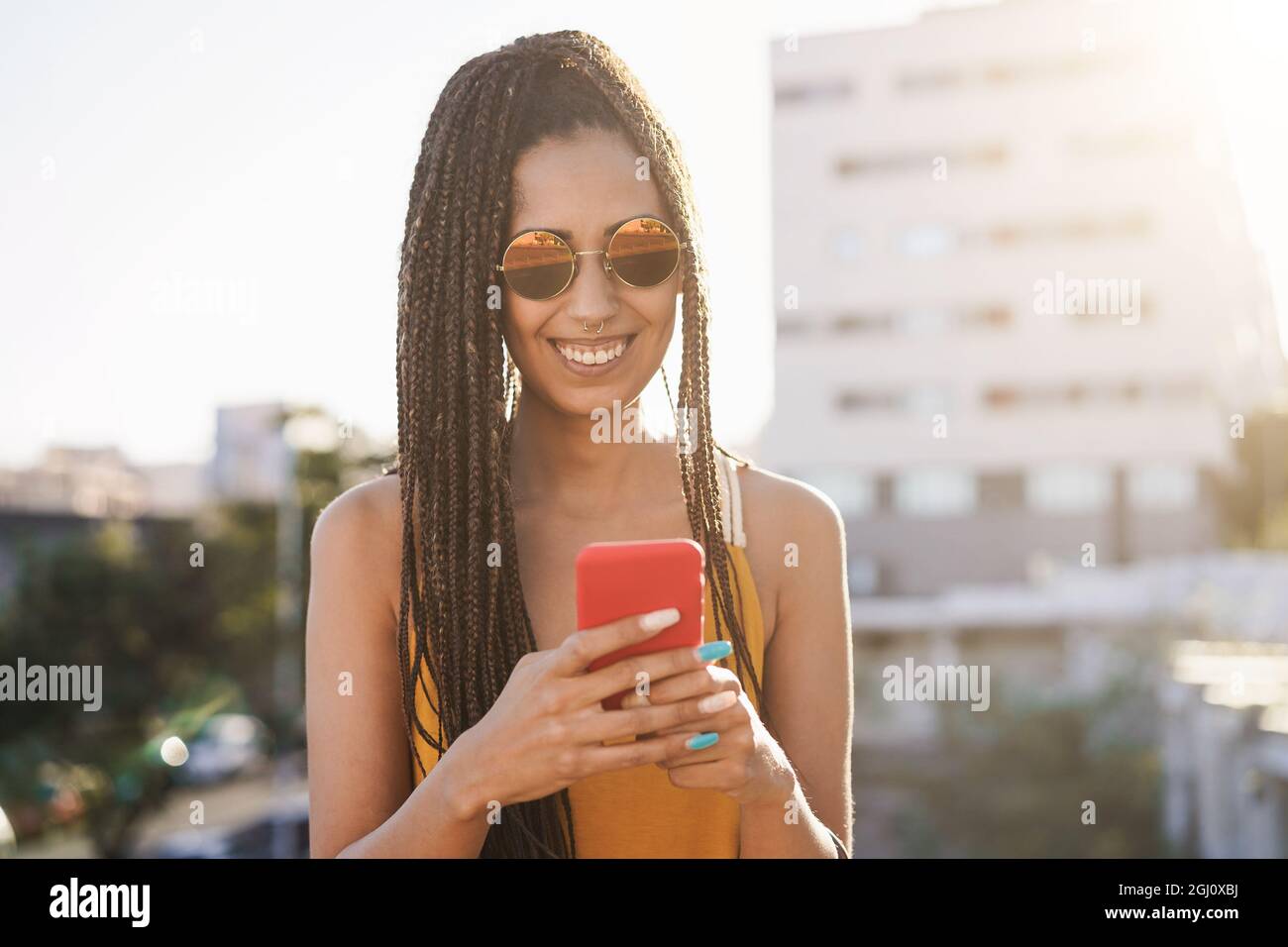 Bohemian african girl using mobile phone outdoor with city in background - Focus on face Stock Photo