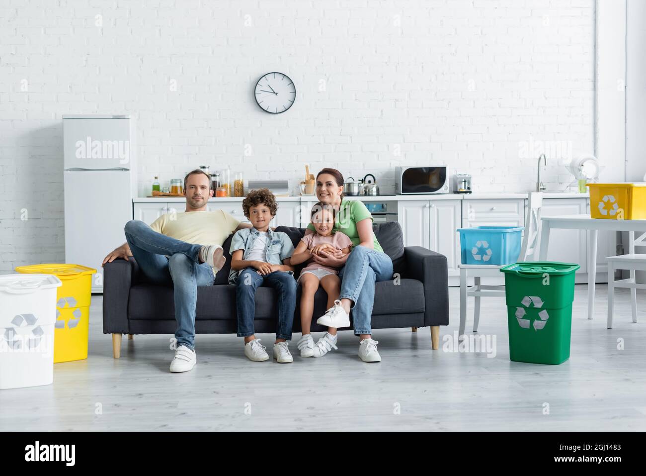 Happy family sitting on couch near trash bins and boxes with recycle