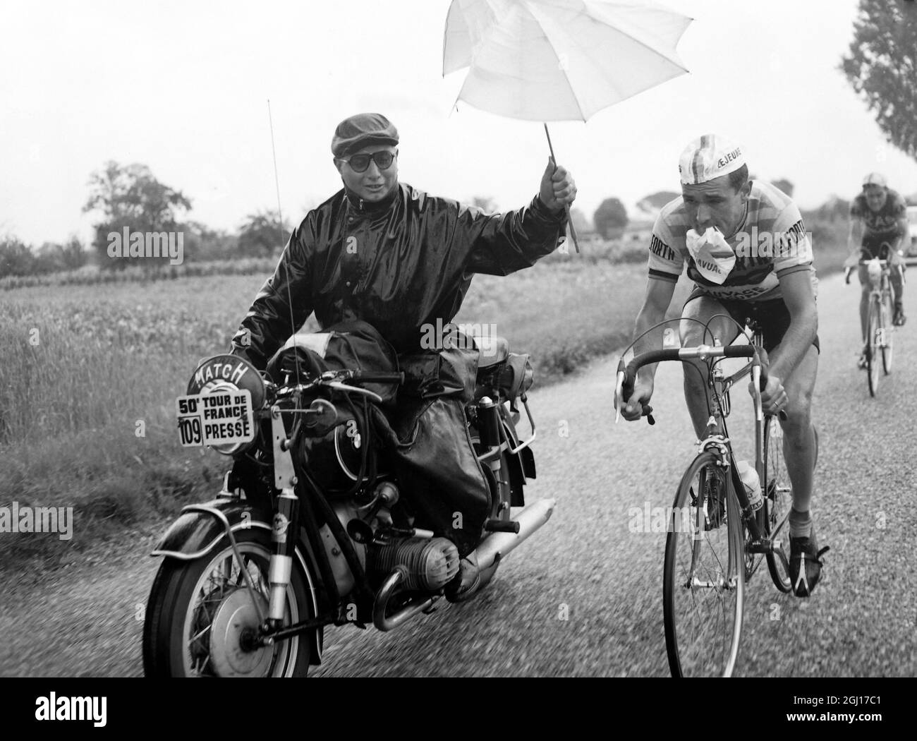 2 JULY 1963 FRENCH CYCLIST HENRI ANGLADE WITH A SUPPORT RIDER ATTEMPTING TO KEEP THE DRIVING RAIN OFF WITH AN UMBRELLA DURING A STAGE OF THE TOUR DE FRANCE IN BORDEAUX, FRANCE. Stock Photo