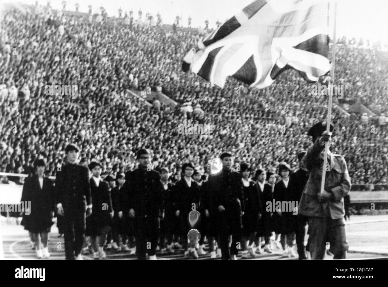 OLYMPICS, OLYMPIC SPORT GAMES - THE XVIII 18TH OLYMPIAD IN TOKYO, JAPAN - JAPANESE STANDARD BEARER CARRIES UNION JACK LED CHILDREN ; 3 OCTOBER 1964 Stock Photo