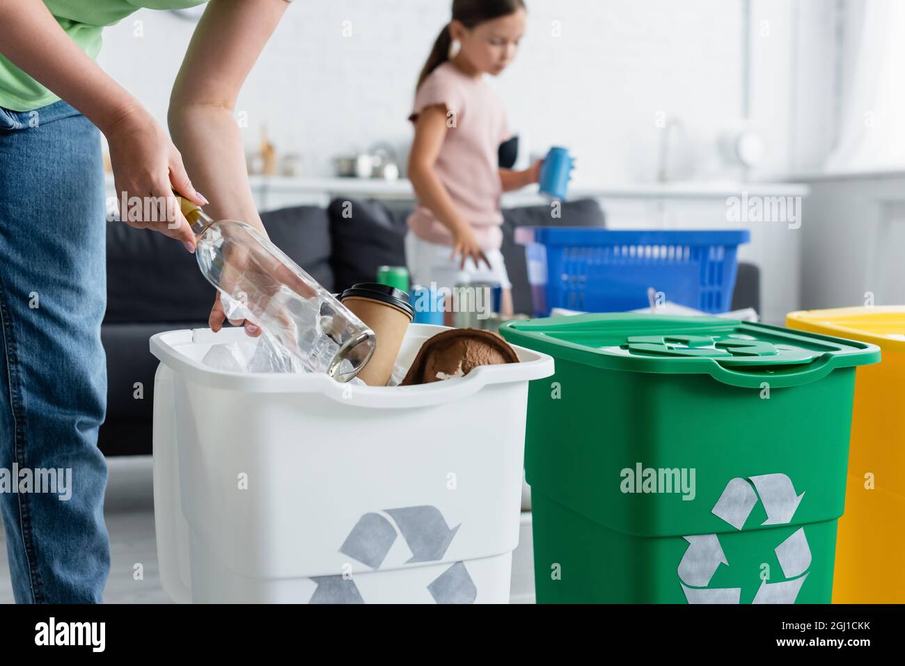 Woman holding bottle near trash can with recycle sign at home Stock Photo