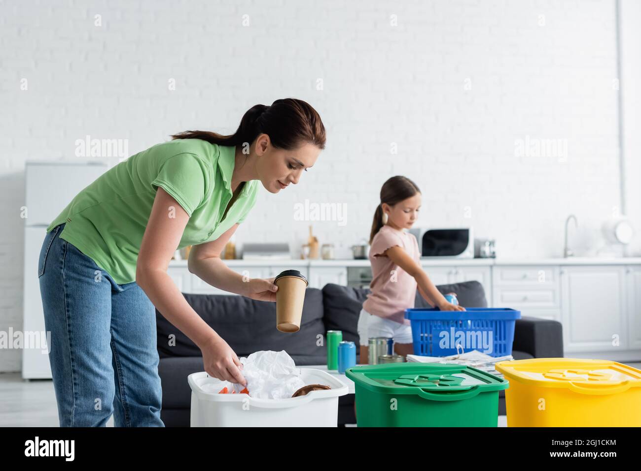 Woman holding paper cup near trash can and daughter at home Stock Photo