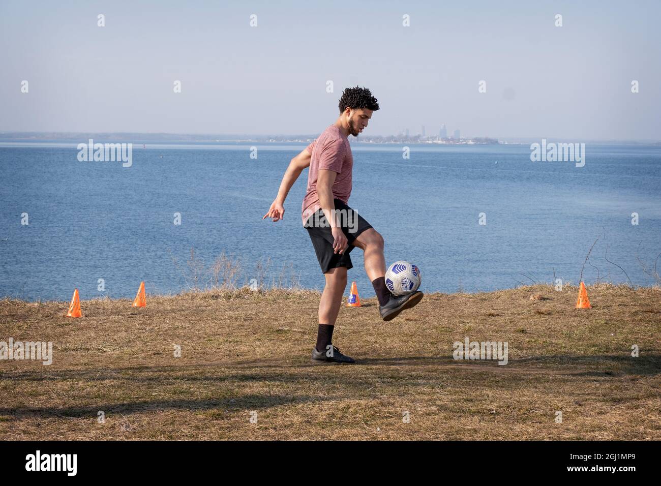 A collegiate varsity soccer plays practices ball handling at a scenic spot in Little Bay Park, Whitestone, Queens, New York City. Stock Photo
