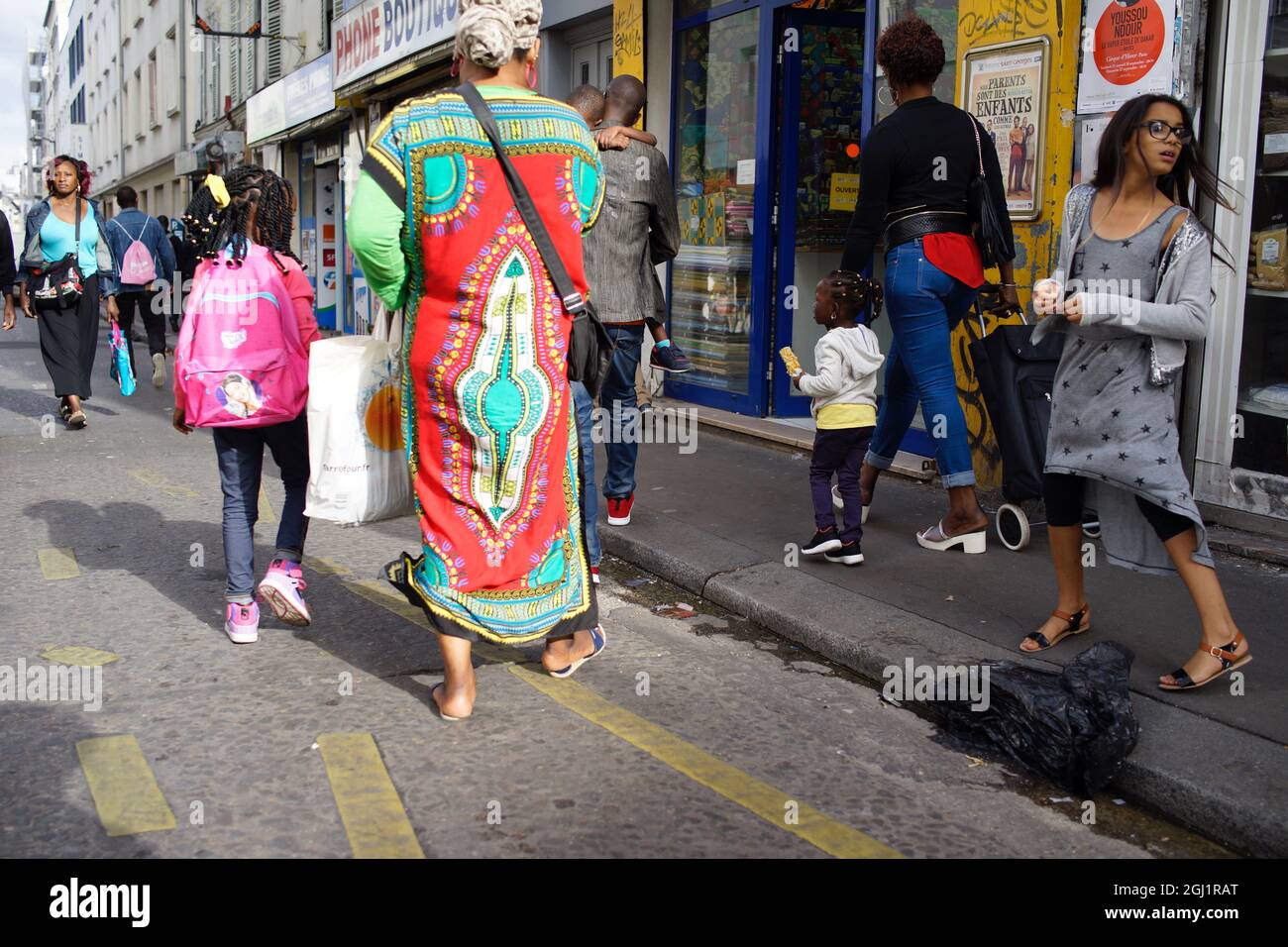 West African woman in traditional Dashiki dress, walking on a busy rue Myrha, La Goutte dOr, Château-Rouge, Paris, 75018, France Stock Photo