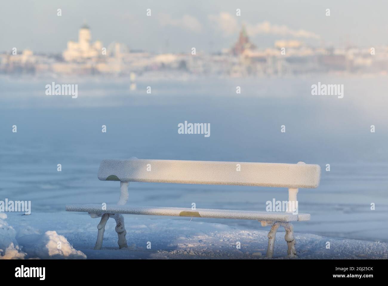 Traditional wooden and frosty resting bench in Helsinki, Finland  on extremely cold winter morning with freezing Baltic Sea and downtown Helsinki skyl Stock Photo