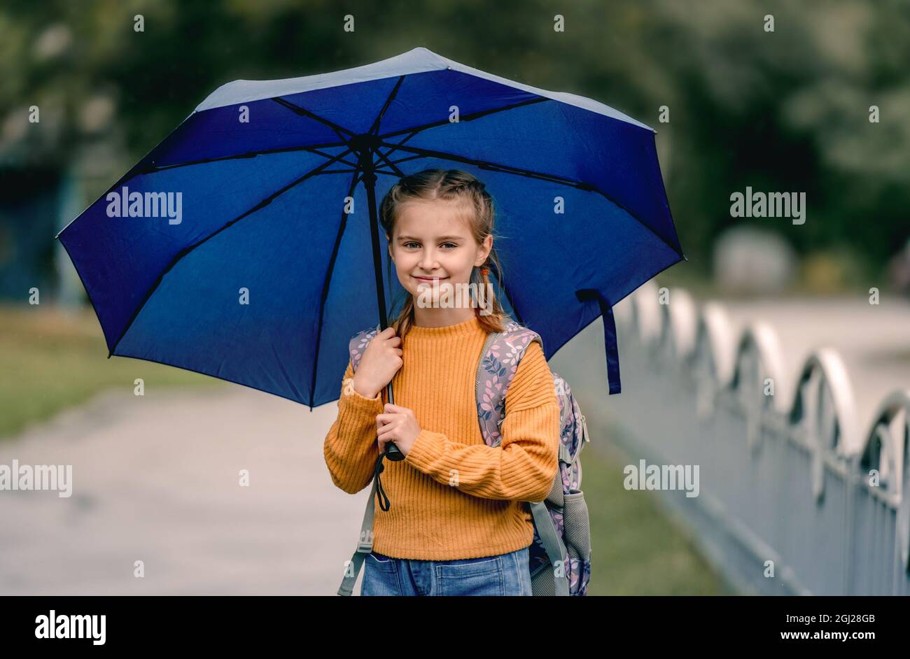 School girl with backpack and umbrella outdoors. Pretty child kid ...