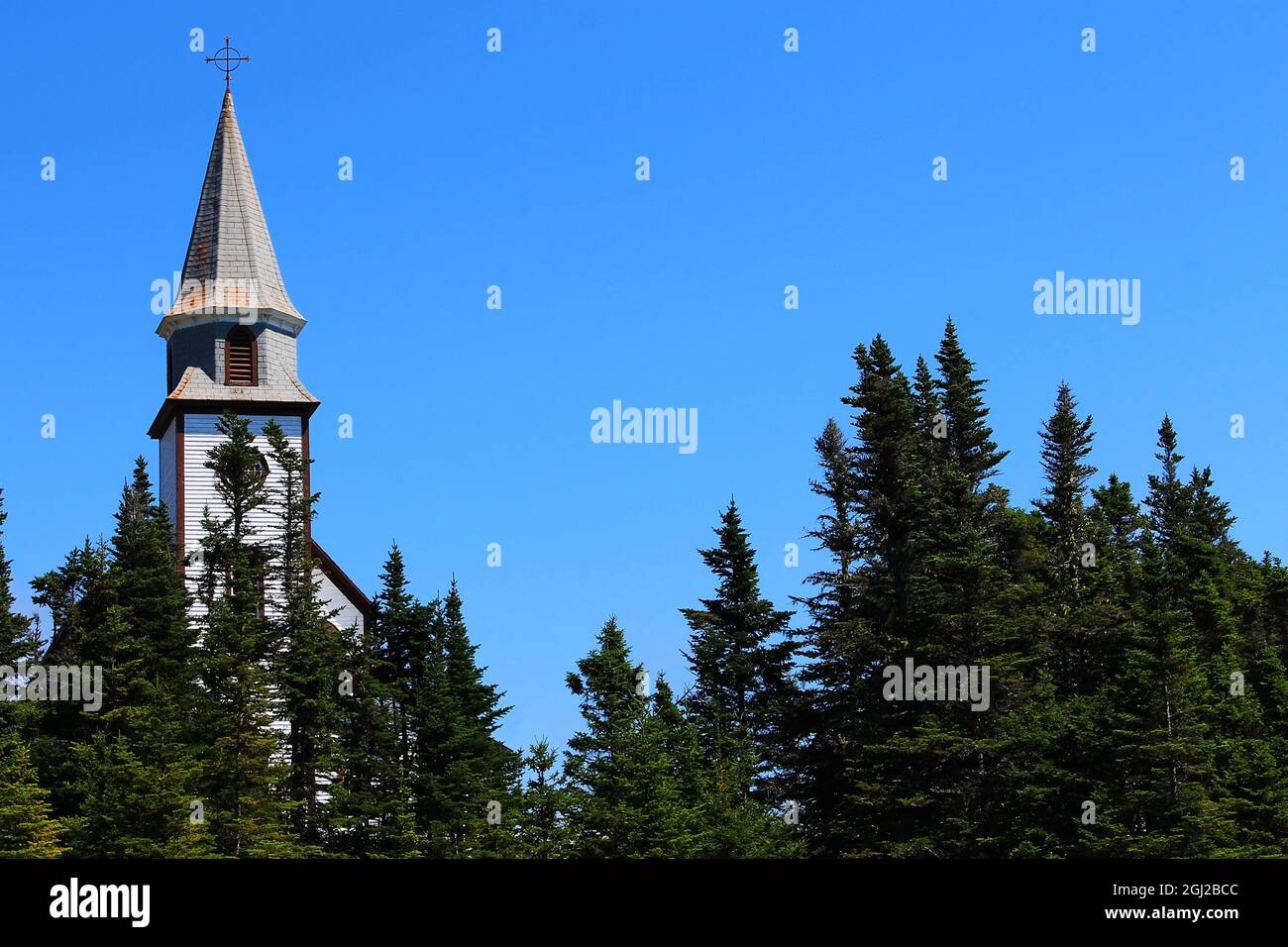 A church steeple, from an old, wooden, rural church, rising above the trees. Stock Photo