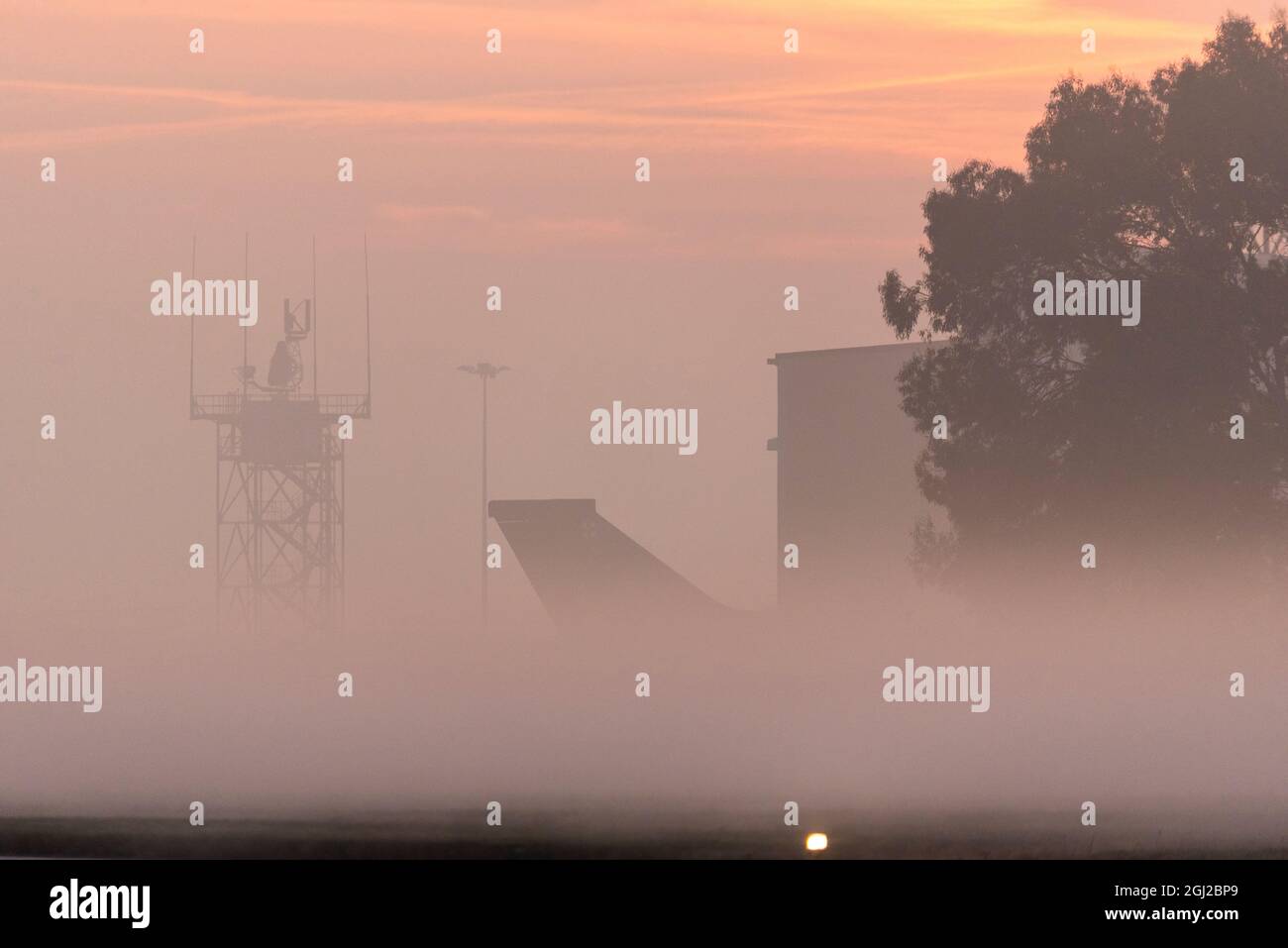 Plane fin, hangar and radar tower at London Southend Airport, Essex, UK, early in the morning with low lying mist at sunrise. Misty dawn Stock Photo